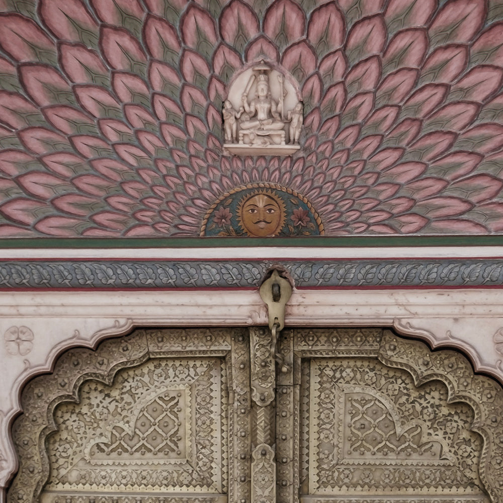 Close-up detail showing the pink lotus petal fan, painted sun face and carved brass door panels